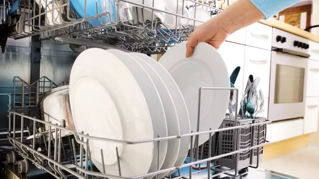 Mão organizando pratos dentro de uma máquina lava-louças