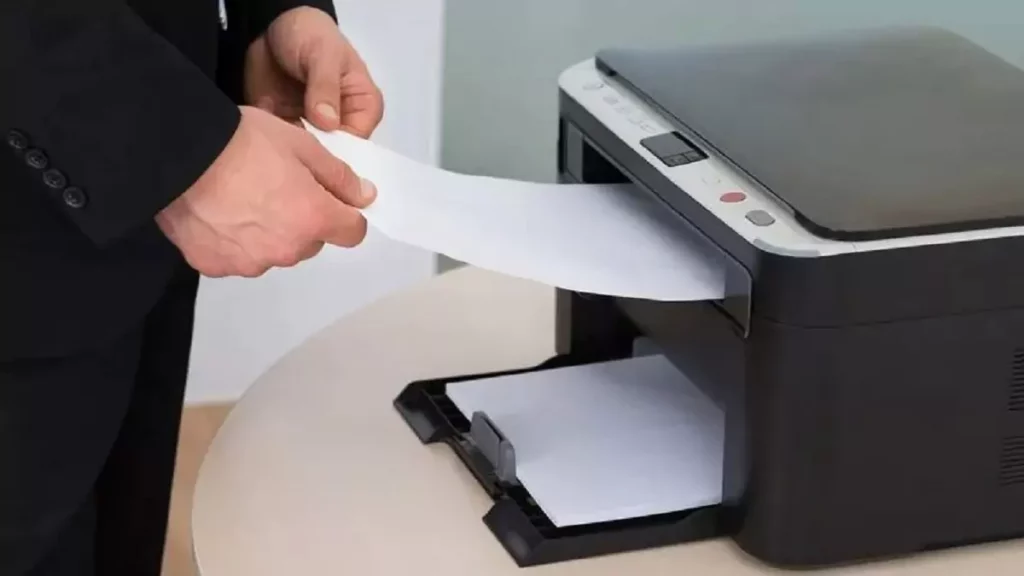 Foco em mão masculina retirando impressão de dentro de uma impressora laser