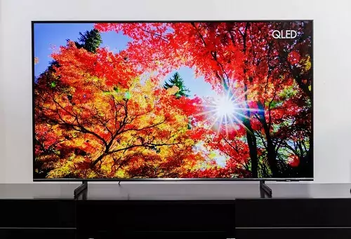 Samsung Q60B em cima de rack marrom com uma paisagem de floresta no outono sendo reproduzida