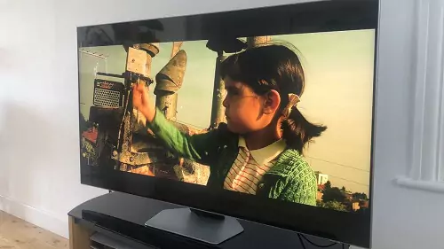 Samsung QN85B em cima de rack marrom com imagem de menina sendo reproduzida na tela