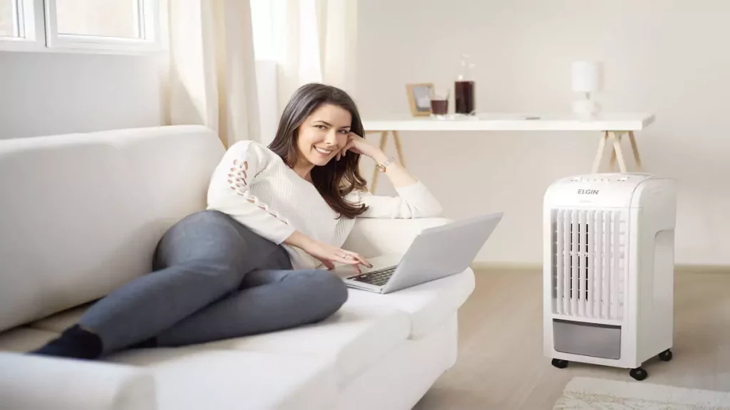 Imagem de abertura do post sobre gasto de energia do climatizador: Mulher no sofá ao lado de climatizador