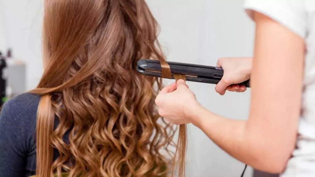 Abertura do post sobre como enrolar cabelo com Chapinha: Cabelereira enrolando o cabelo de mulher com prancha