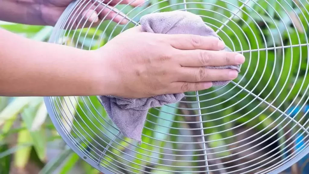 Abertura do post sobre como limpar ventilador: Mão limpando grade de ventilador