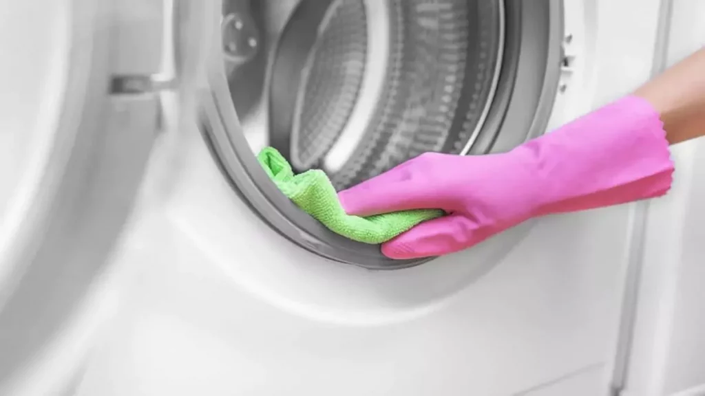 Abertura do post sobre como limpar máquina de lavar: Mão vestida com luva limpando porta de lavadora.