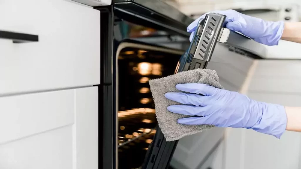Abertura do post sobre como limpar fogão: Mão vestida de luva limpando porta de fogão
