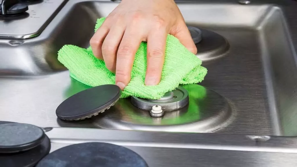 Mão limpando boca de fogão com flanela verde