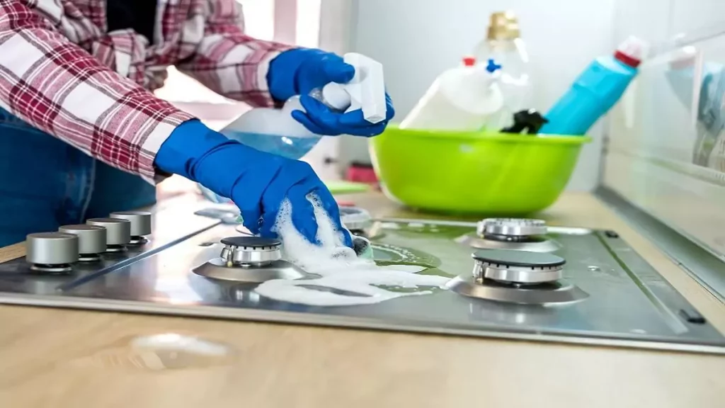 Pessoa com luvas azuis usando mistura caseira para limpar fogão